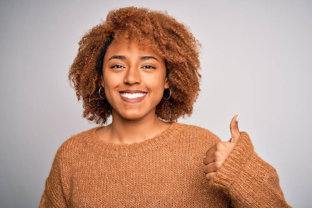 Νεαρή όμορφη Αφρο-αμερικανική γυναίκα με σγουρά μαλλιά φορώντας casual πουλόβερ ευτυχισμένη με μεγάλο χαμόγελο κάνει ok σημάδι, τον αντίχειρα επάνω με τα δάχτυλα, εξαιρετική πινακίδα - Φωτογραφία, εικόνα