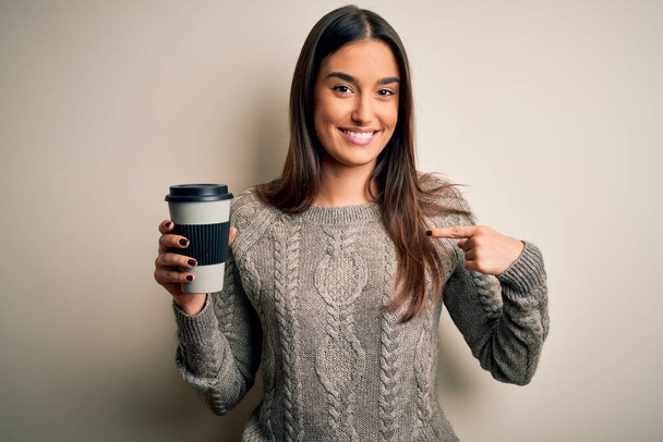 Молодая красивая брюнетка женщина пьет кофе на изолированном белом фоне с удивленным лицом указывая пальцем на себя
 - Фото, изображение