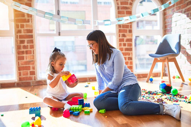 Καυκάσιο κορίτσι παίζει και μαθαίνει στο σχολείο με μια δασκάλα. Μητέρα και κόρη στο playroom γύρω από παιχνίδια που παίζουν με ογκόλιθους - Φωτογραφία, εικόνα