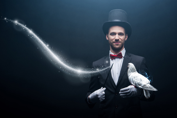 mágico feliz em chapéu fazendo abracadabra com pomba e varinha em quarto escuro com fumaça e ilustração brilhante
 - Foto, Imagem