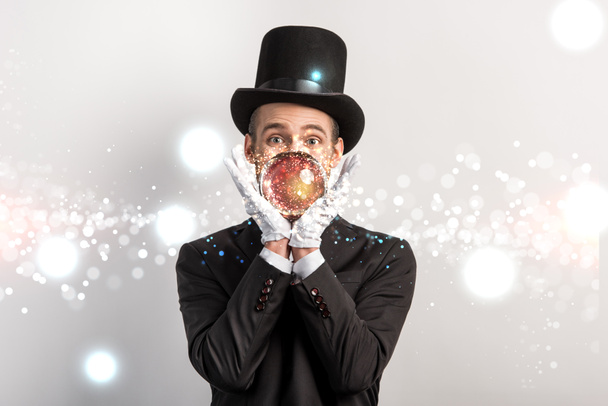 professional magician holding magic ball isolated on grey with glowing illustration - Photo, Image
