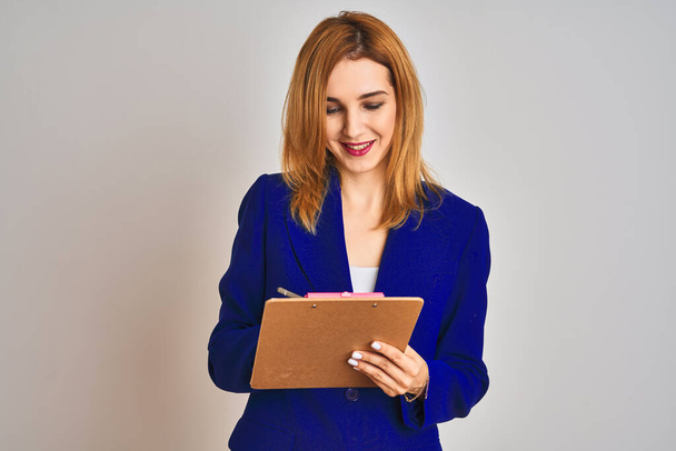 Redhead business caucasian woman holding clipboard over isolated background with a happy face standing and smiling with a confident smile showing teeth - Photo, Image
