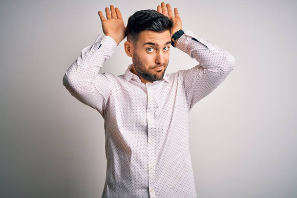 Young handsome man wearing elegant shirt standing over isolated white background Doing bunny ears gesture with hands palms looking cynical and skeptical. Easter rabbit concept. - Fotoğraf, Görsel