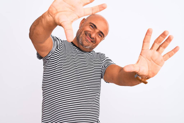 Красивый мужчина средних лет в полосатой морской футболке на изолированном белом фоне делает рамку с помощью ладоней и пальцев, камеры перспективы
 - Фото, изображение
