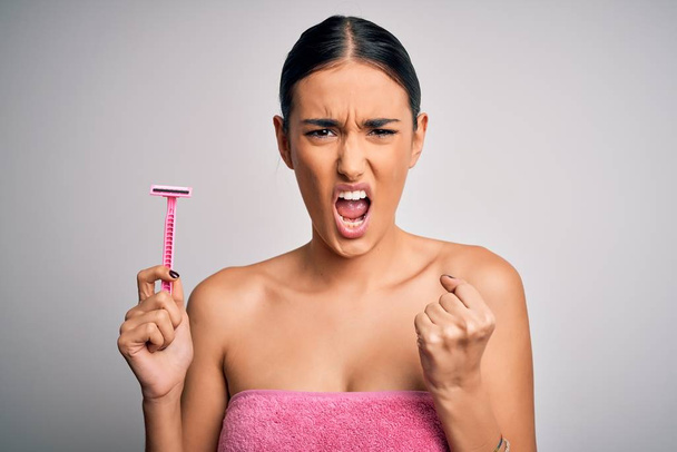 Young beautiful brunette woman wearing towel using razor for depilation annoyed and frustrated shouting with anger, crazy and yelling with raised hand, anger concept - Fotoğraf, Görsel
