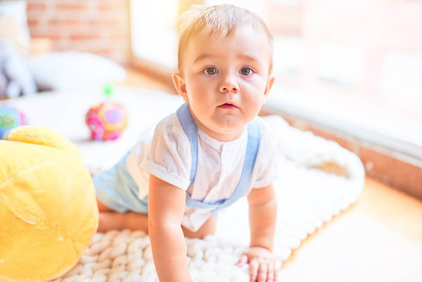 Красивый малыш, сидящий на одеяле и играющий с уткой в детском саду
 - Фото, изображение