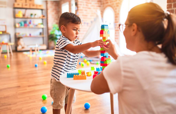 Beautiful teacher and toddler boy playing with construction blocks bulding tower at kindergarten - Foto, immagini