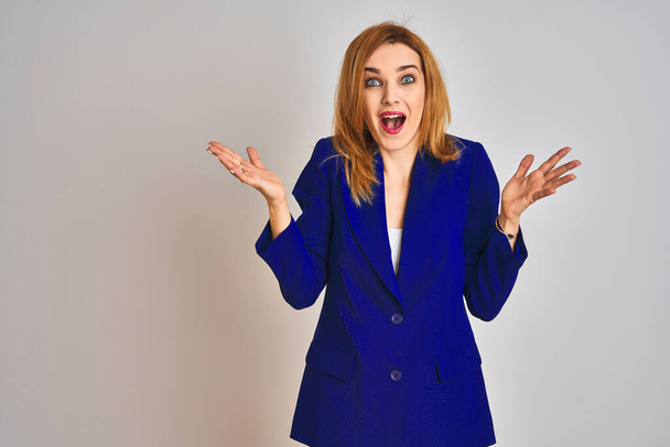 Redhead caucasian business woman wearing a suit over isolated background celebrating crazy and amazed for success with arms raised and open eyes screaming excited. Winner concept - Fotografie, Obrázek