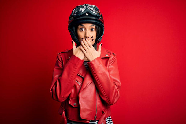 Joven hermosa morena motociclista mujer con casco de moto y chaqueta roja impactada cubriendo la boca con las manos por error. Concepto secreto
. - Foto, Imagen