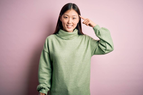 Young beautiful asian woman wearing green winter sweater over pink solated background Smiling pointing to head with one finger, great idea or thought, good memory - Zdjęcie, obraz