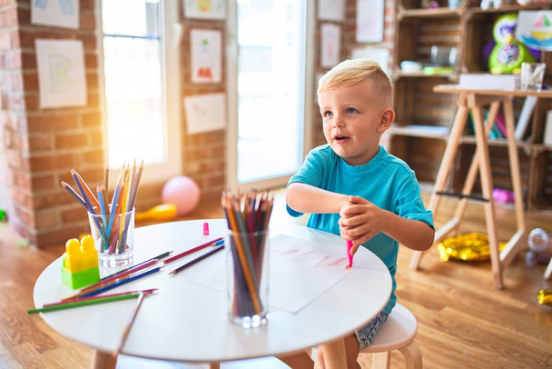 Молодой кавказский ребенок играет в детском саду, рисуя цветными карандашами. Дошкольный мальчик счастлив в игровой комнате
. - Фото, изображение