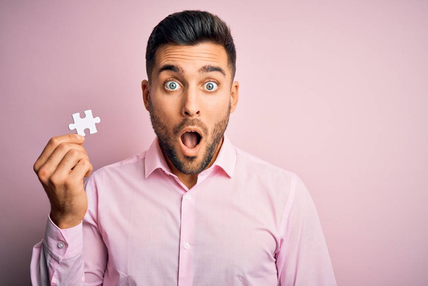 Young handsome businessman holding piece of puzzle over isolated pink background scared in shock with a surprise face, afraid and excited with fear expression - Fotoğraf, Görsel