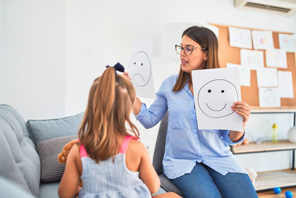 Young therapist woman speaking and treating child, counselor and behaviour correction at pedagogue payroom showing happy and sad faces - Foto, imagen