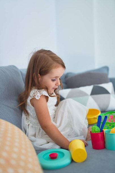 entzückende blonde Kleinkind sitzt auf dem Sofa Kochen mit Essen und Besteck Spielzeug zu Hause - Foto, Bild