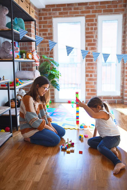 Bela professora e criança brincando com blocos de madeira treinar em torno de lotes de brinquedos no jardim de infância
 - Foto, Imagem
