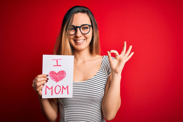 Молодая красивая женщина держит бумагу с любовью мама сообщение празднование Дня матери делает хорошо знак с пальцами, отличный символ
 - Фото, изображение