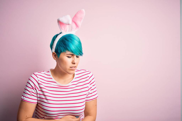 Jeune femme aux cheveux bleus mode portant des oreilles de lapin de Pâques sur fond rose avec la main sur le ventre parce que l'indigestion, la maladie douloureuse se sentent mal. Concept Ache
. - Photo, image