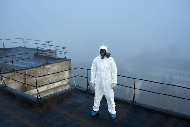 Koruyucu kıyafetli bir insan, sisli havada çatıdaki kameranın merkezinde kirlilik araştırması yapıyor. - Fotoğraf, Görsel