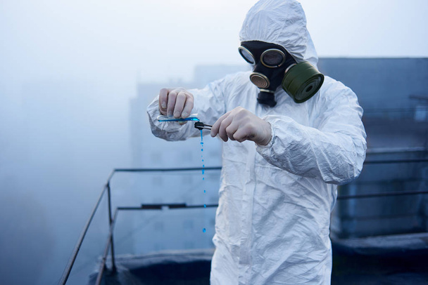 Investigación científica sobre un tema entorno peligroso, llevada a cabo por un trabajador de laboratorio en traje de protección en el techo del edificio, que posee el equipo adecuado
 - Foto, imagen