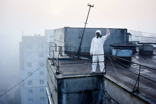 Wissenschaftler in Schutzanzug steht auf dem Dach, umgeben von Stromleitungen, zeigt Stoppschild, Gebäude im Hintergrund - Foto, Bild