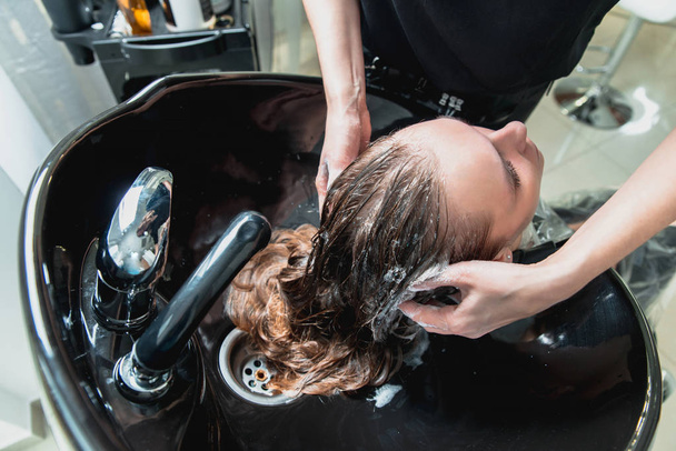 Friseur wäscht Haare eines blonden Mädchens im Friseursalon vor dem Haarschnitt - Foto, Bild