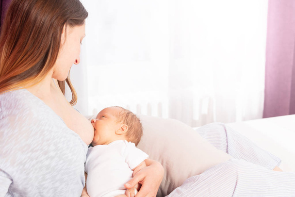 Newborn baby breastfeeding with mother sit on bed - 写真・画像