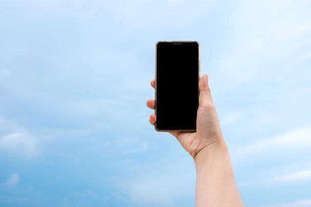 Mano de mujer sosteniendo teléfono inteligente con cielo azul y fondo de nube. Pantalla de visualización de ruta de recorte incluyen en esta imagen
. - Foto, imagen