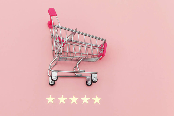 Pequeño supermercado carrito de compras empuje para juguete de compras con ruedas y clasificación de 5 estrellas aislado sobre fondo rosa pastel. Compras al por menor concepto de evaluación y revisión en línea
. - Foto, imagen