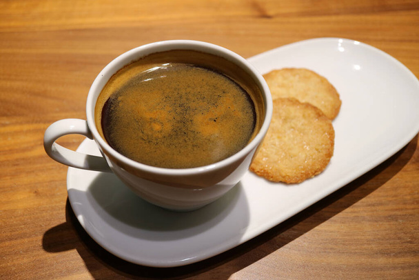 Κύπελλο του μαύρου καφέ με μερικά cookies σερβίρεται σε ξύλινο τραπέζι - Φωτογραφία, εικόνα