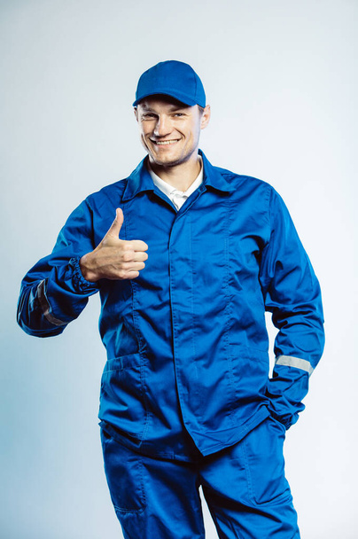 Portrait of young worker man wearing blue uniform. Showing thumb up. Movement cool. Isolated on grey background with copy space. Human face expression, emotion. Business concept. - Fotó, kép