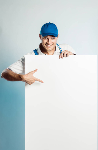 Mockup image of a young smiling worker holding empty white banner and points to it. - Φωτογραφία, εικόνα