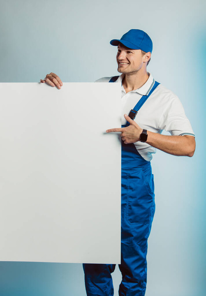Mockup image of a young smiling worker holding empty white banner and points to it. - Fotoğraf, Görsel