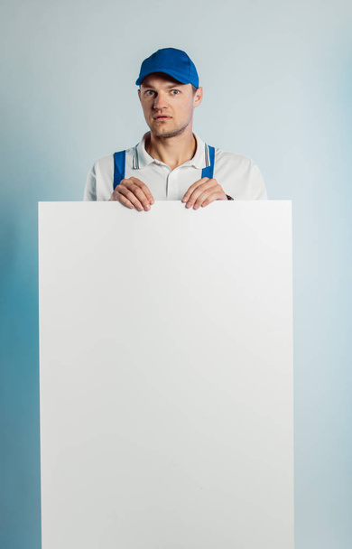 Mockup image of a young surprised worker holding empty white banner. White or blue background. Business concept. - Foto, immagini