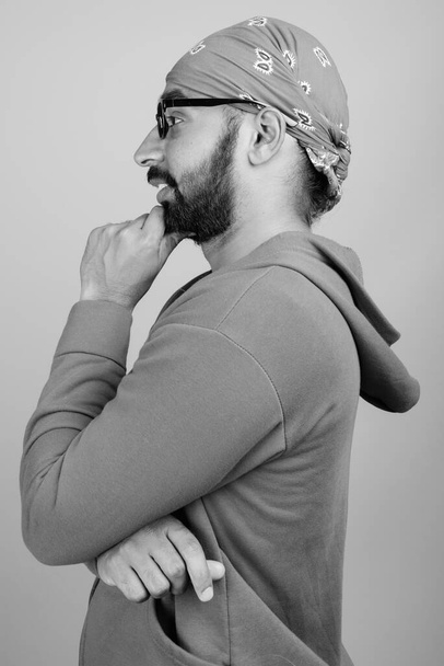 Studio shot of young handsome bearded Indian man wearing eyeglasses against gray background in black and white - Foto, Imagen
