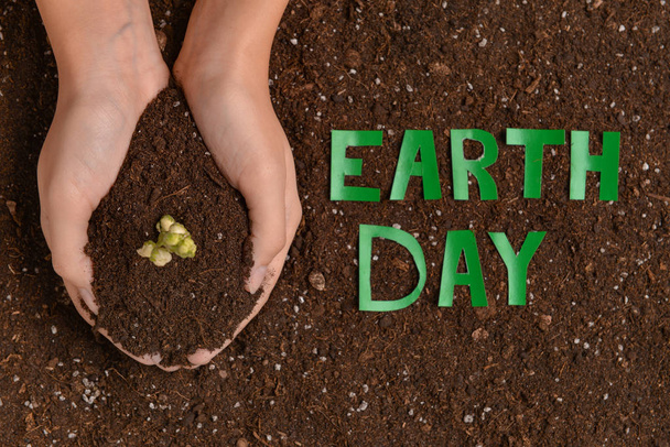 Weibliche Hände mit Erde und Text Earth Day - Foto, Bild