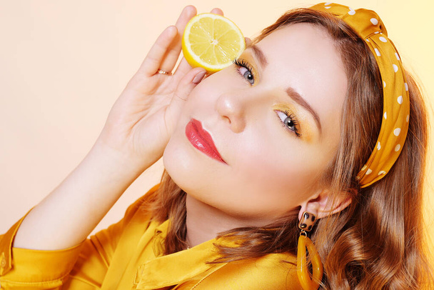 Beautiful girl, yellow make-up, bright colors. Girl holds lemons - Photo, Image