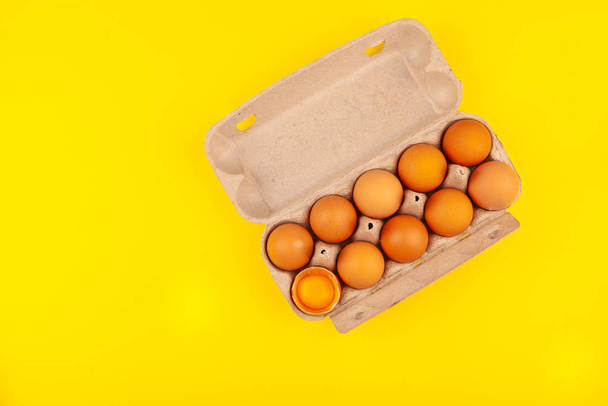 卵チキン卵。茶色の卵を持つ開いた灰色の箱のトップビュー黄色の背景に隔離されています。1個の卵は半分に割れ、黄色い丸黄身です。純粋なタンパク質を得るという健康的なライフスタイルの概念 - 写真・画像