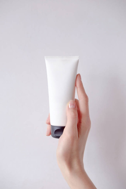 Young female hand holds minimalistic mockup cosmetic packaging. Mock-up for branding and label. - 写真・画像