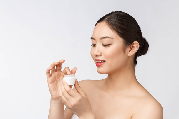 Beautiful young woman on white isolated background holding cosmetic face cream, asian - Foto, afbeelding