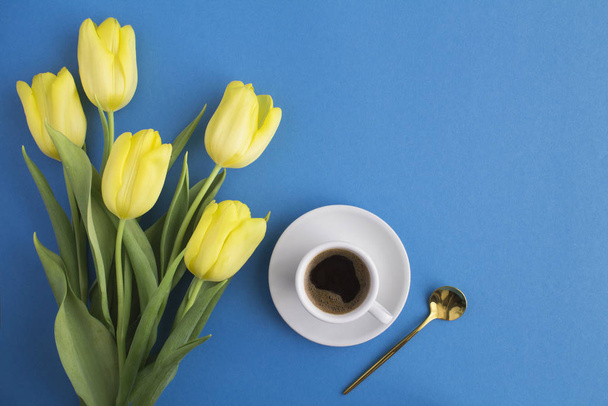 Черный кофе в белой чашке и желтые тюльпаны на синем фоне. Копирование пространства
. - Фото, изображение