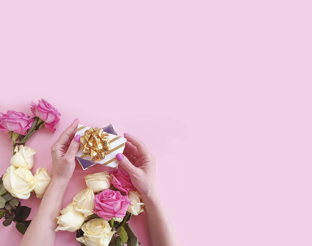 hands holding a gift box, a bouquet of roses on a colored background - Foto, imagen