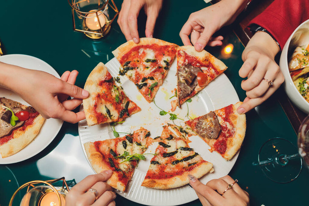 Flat lay with traditional Italian pizza with mussels, arugula and parmesan on dark blue stone table. Friends eating pizza. Peoples hands grabbing a slice of pizza. - Foto, afbeelding