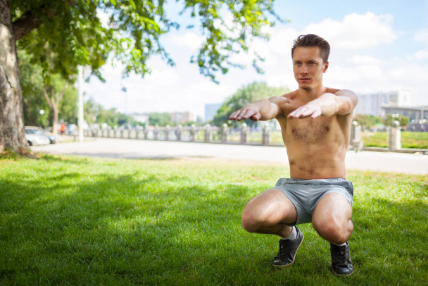 Shirtless young man doing squats. - Foto, afbeelding