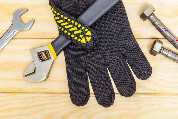 Plumbing equipment repair tools adjustable wrench and hose, gloves, flexible connection on wooden boards - 写真・画像