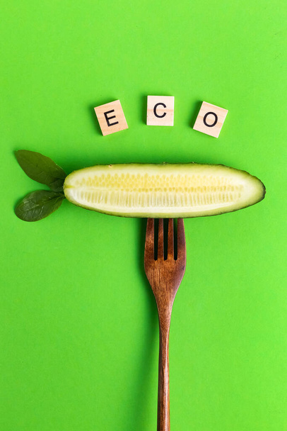 Letters vegan vegan healthier eco cucumber on a wooden fork on a green background - Photo, image