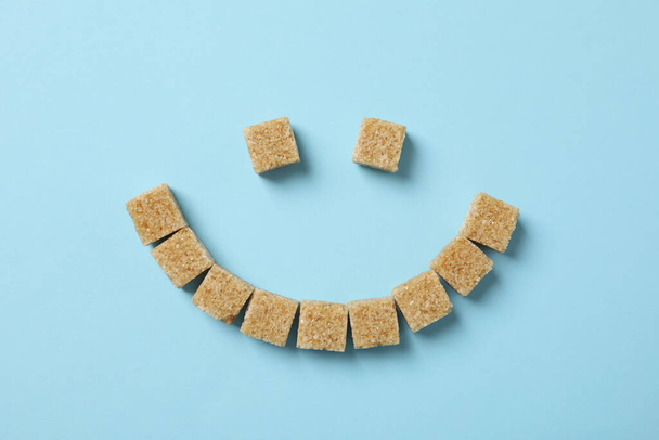 Cara sonriente hecha de cubos de azúcar sobre fondo azul, vista superior
 - Foto, imagen