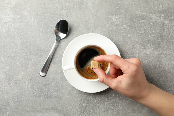 Female hand holding sugar cube on grey background with cup of co - Zdjęcie, obraz
