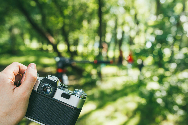 a mans hand holds an old vintage film camera and photographs a green landscape. first-person view POV - Photo, Image
