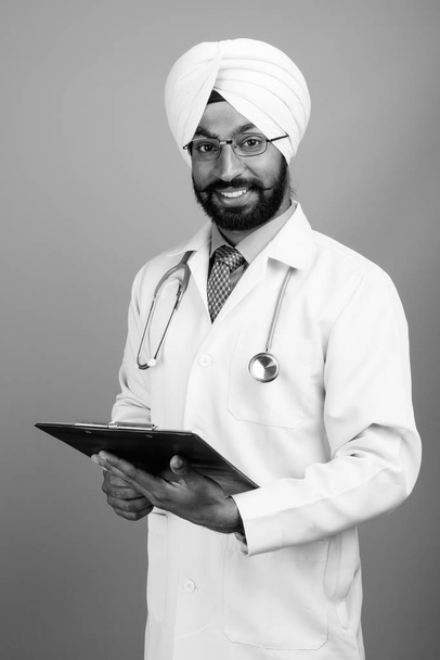 Studio shot of young handsome bearded Indian Sikh man doctor against gray background in black and white - Fotografie, Obrázek