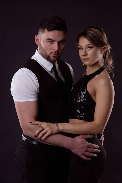 A woman in a black dress and a brutal man on a black background - Foto, Imagen